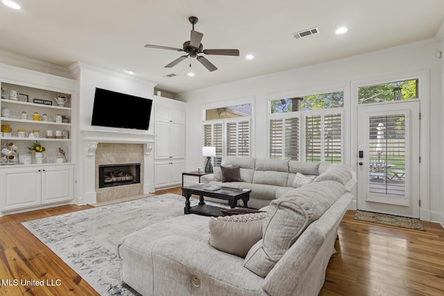 living area featuring ceiling fan, visible vents, crown molding, a fireplace, and light wood-style floors