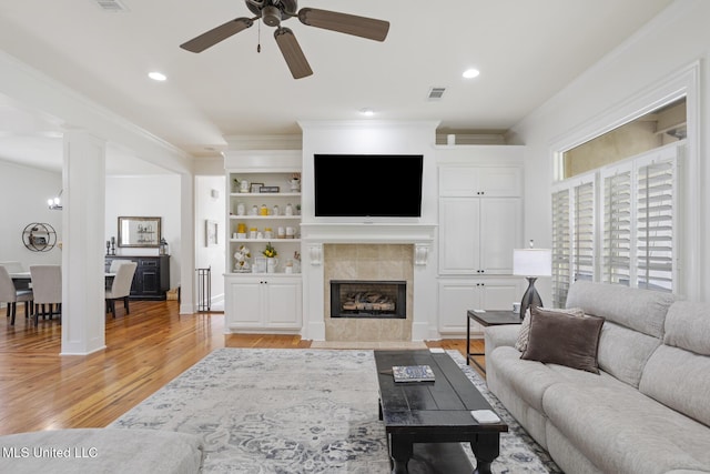 living room with visible vents, ornamental molding, ceiling fan, light wood-type flooring, and a tiled fireplace