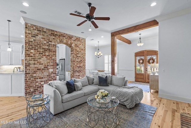 living area featuring arched walkways, brick wall, visible vents, and light wood finished floors