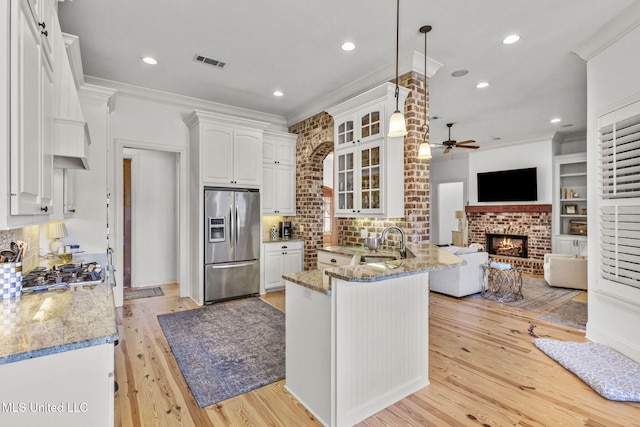 kitchen featuring stainless steel appliances, visible vents, glass insert cabinets, ornamental molding, and a sink