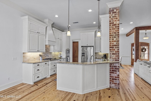 kitchen with appliances with stainless steel finishes, white cabinets, a peninsula, and custom exhaust hood