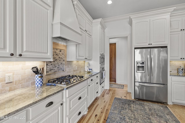 kitchen with appliances with stainless steel finishes, custom exhaust hood, white cabinets, and light wood-style floors