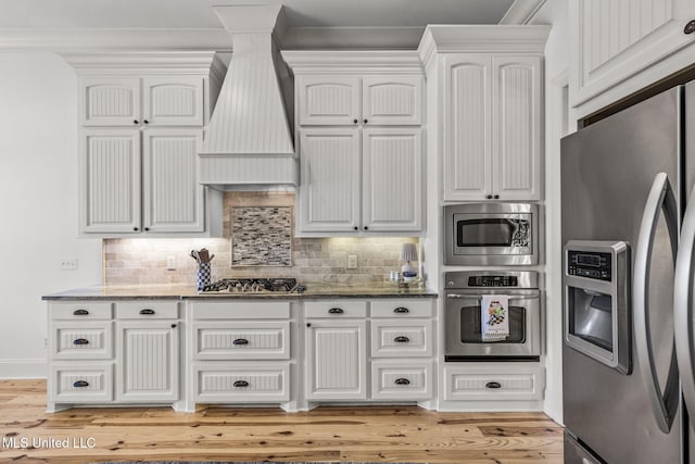 kitchen with appliances with stainless steel finishes, stone countertops, white cabinets, and custom range hood