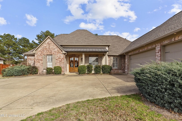 view of front of property featuring a shingled roof, metal roof, an attached garage, french doors, and brick siding