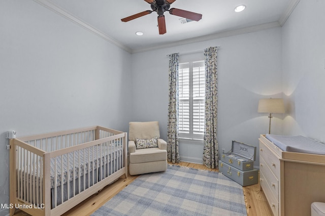 bedroom featuring a nursery area, light wood finished floors, recessed lighting, and crown molding