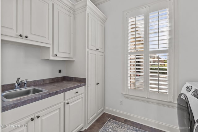 kitchen featuring washing machine and dryer, a sink, baseboards, white cabinets, and dark countertops