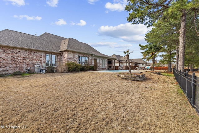 back of house with a shingled roof, brick siding, fence, and a lawn