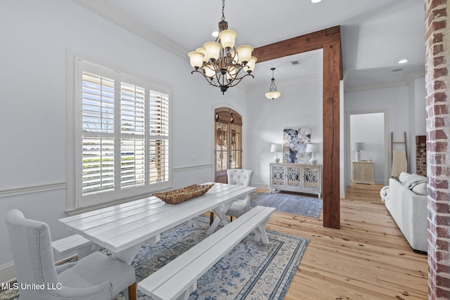 dining room featuring ornamental molding, arched walkways, an inviting chandelier, and wood finished floors