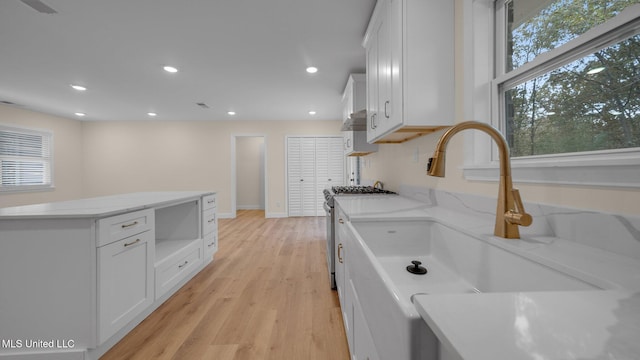 kitchen with light wood-type flooring, white cabinetry, stainless steel gas stove, and light stone counters