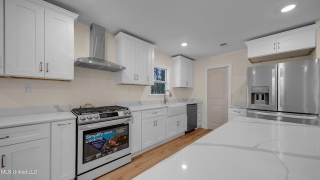 kitchen with white cabinetry, light wood-type flooring, appliances with stainless steel finishes, and wall chimney range hood