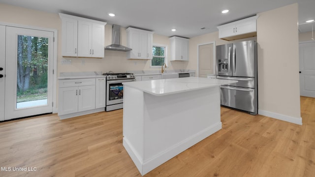 kitchen featuring appliances with stainless steel finishes, wall chimney exhaust hood, light hardwood / wood-style floors, and white cabinets