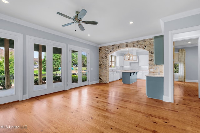 unfurnished living room featuring ornamental molding, sink, ceiling fan with notable chandelier, and light wood-type flooring