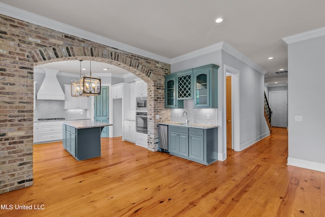 kitchen with a kitchen island, appliances with stainless steel finishes, custom range hood, light hardwood / wood-style floors, and sink