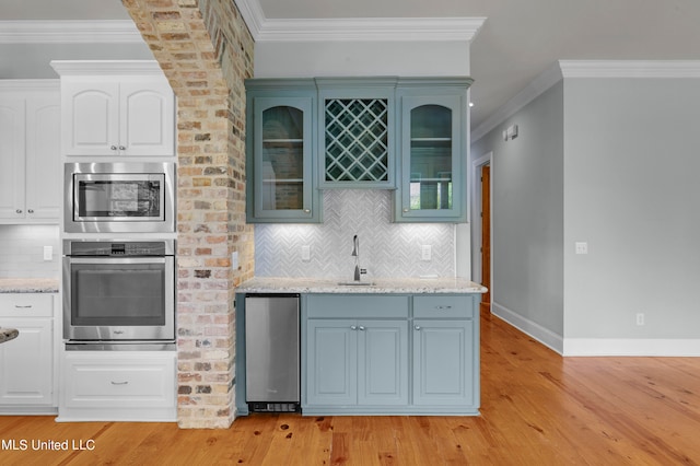 kitchen featuring appliances with stainless steel finishes, white cabinetry, light hardwood / wood-style flooring, ornamental molding, and sink