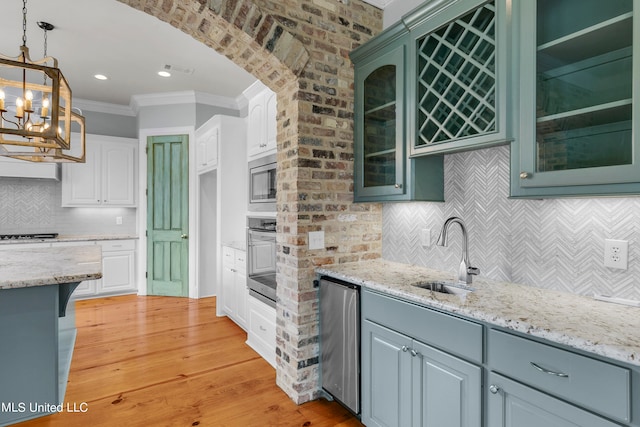 kitchen with decorative backsplash, white cabinets, appliances with stainless steel finishes, light wood-type flooring, and sink