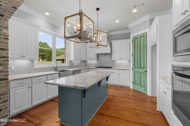 kitchen with white cabinets, a kitchen island, light hardwood / wood-style flooring, pendant lighting, and light stone counters