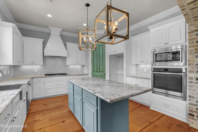 kitchen featuring a kitchen island, pendant lighting, custom exhaust hood, appliances with stainless steel finishes, and light hardwood / wood-style floors