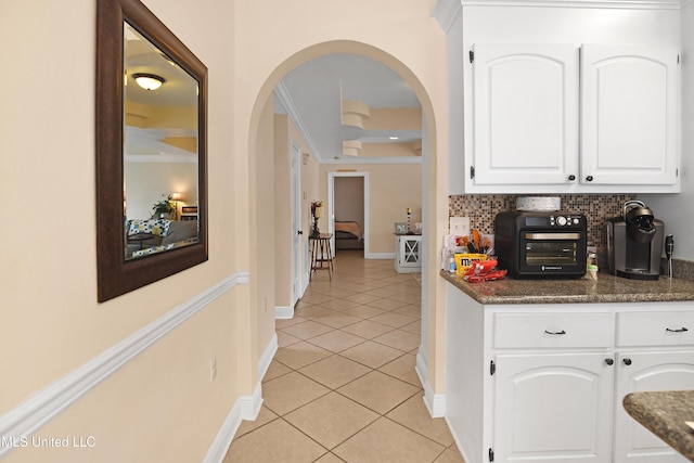 kitchen featuring tasteful backsplash, white cabinetry, dark stone countertops, ornamental molding, and light tile patterned floors