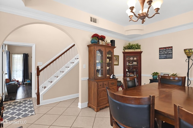 tiled dining space with an inviting chandelier, ornamental molding, and a tray ceiling