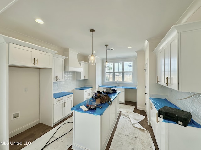 kitchen featuring tasteful backsplash, wall chimney range hood, pendant lighting, and white cabinets