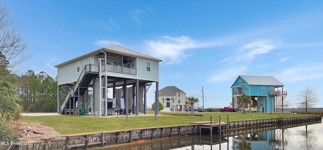 rear view of house with stairs, a yard, and a water view