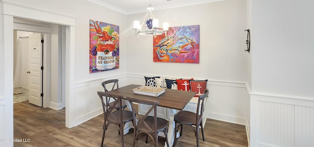 dining room with a wainscoted wall, ornamental molding, wood finished floors, and a notable chandelier