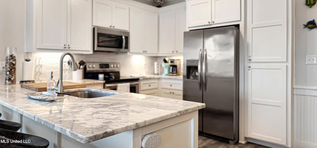 kitchen with stainless steel appliances, white cabinets, a kitchen breakfast bar, and light stone countertops