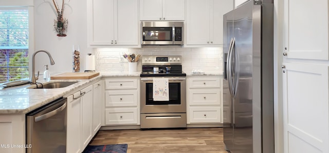 kitchen featuring stainless steel appliances, white cabinetry, a sink, and light stone countertops