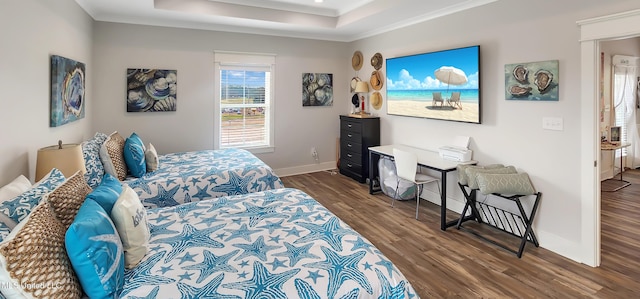 bedroom with ornamental molding, a tray ceiling, dark wood-type flooring, and baseboards