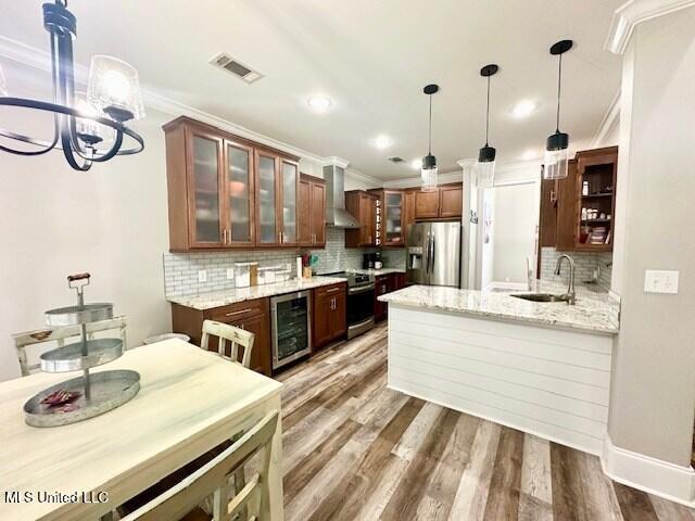 kitchen with wall chimney exhaust hood, dark hardwood / wood-style flooring, pendant lighting, stainless steel appliances, and light stone countertops