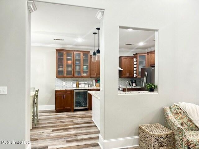 bar featuring pendant lighting, stainless steel fridge, decorative backsplash, beverage cooler, and light wood-type flooring