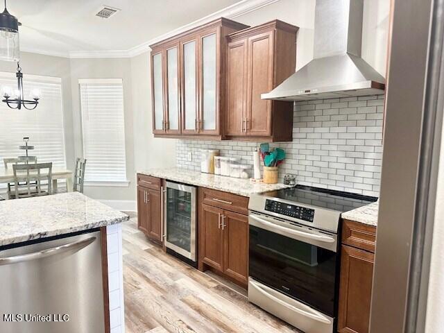 kitchen with decorative light fixtures, stainless steel appliances, beverage cooler, light hardwood / wood-style floors, and wall chimney range hood