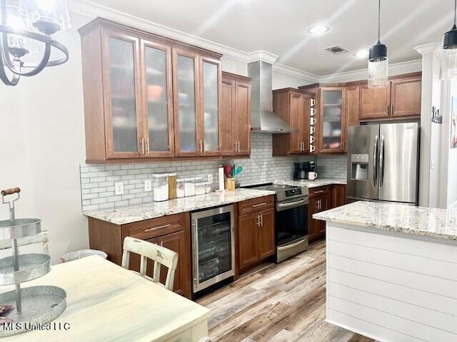 kitchen with wine cooler, wall chimney exhaust hood, light stone counters, hanging light fixtures, and appliances with stainless steel finishes