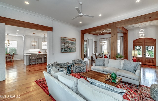 living room with french doors, crown molding, light hardwood / wood-style flooring, and ceiling fan with notable chandelier