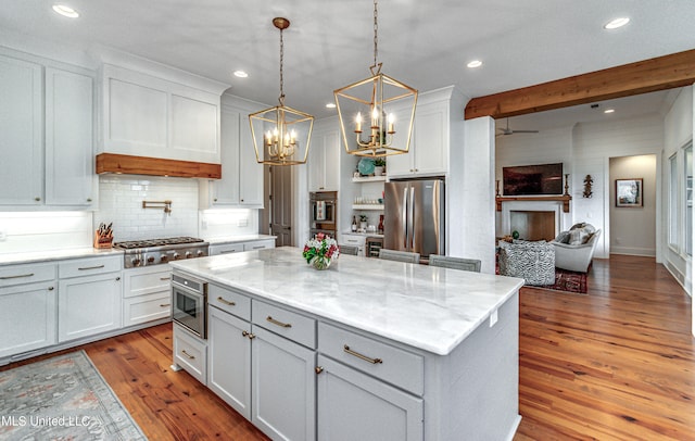 kitchen featuring appliances with stainless steel finishes, wood-type flooring, a kitchen island, white cabinetry, and light stone counters