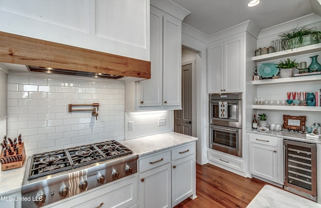 kitchen with stainless steel appliances, hardwood / wood-style floors, light stone countertops, beverage cooler, and white cabinets