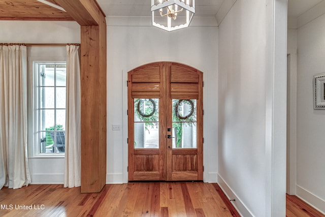 entrance foyer featuring light hardwood / wood-style floors, an inviting chandelier, ornamental molding, and french doors