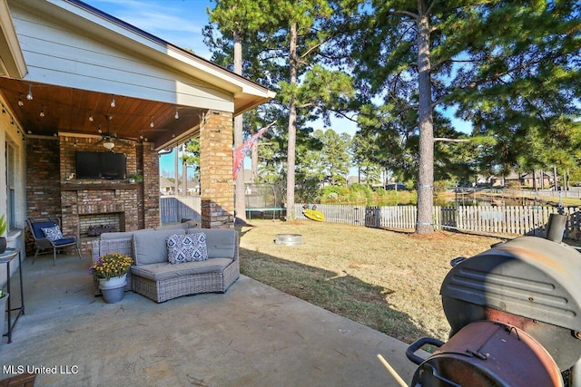 view of patio with ceiling fan, an outdoor living space with a fireplace, a trampoline, and a fenced backyard