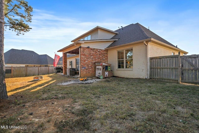 rear view of property featuring a fenced backyard, central air condition unit, brick siding, a yard, and roof with shingles