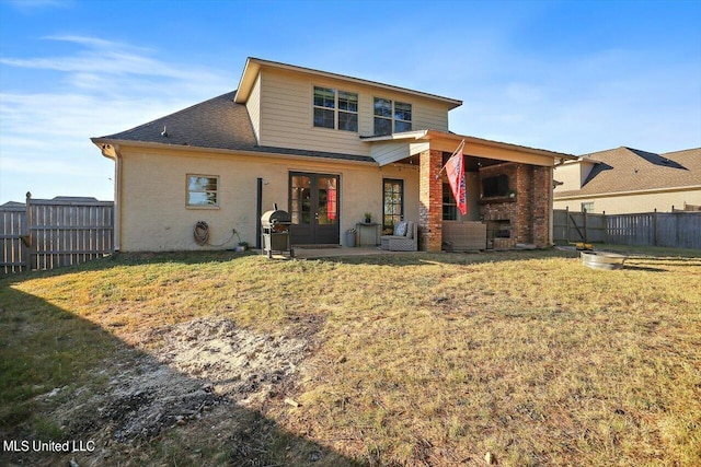 back of house with a yard, a fenced backyard, a fireplace, and french doors