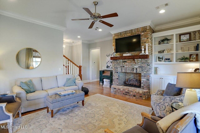 living room with light hardwood / wood-style floors, ornamental molding, ceiling fan, and a brick fireplace