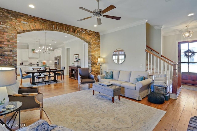 living room with light hardwood / wood-style floors, brick wall, ornamental molding, and ceiling fan with notable chandelier