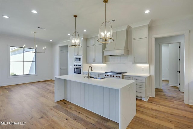 kitchen featuring a sink, light countertops, appliances with stainless steel finishes, custom exhaust hood, and pendant lighting