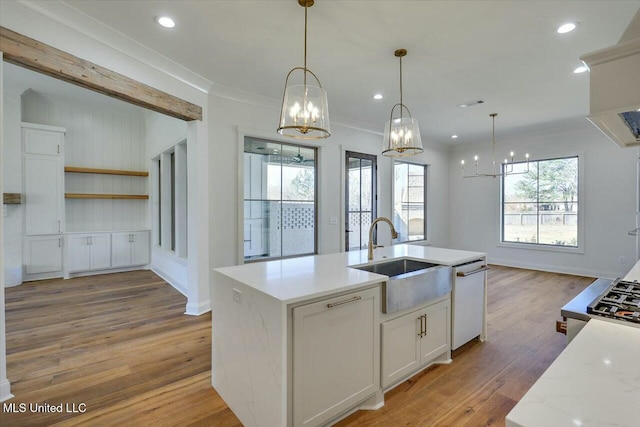 kitchen featuring pendant lighting, a center island with sink, white cabinets, a sink, and light stone countertops