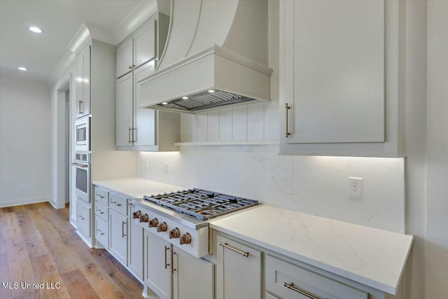 kitchen featuring open shelves, appliances with stainless steel finishes, white cabinetry, light stone countertops, and premium range hood