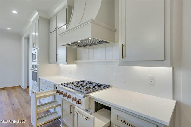 kitchen featuring decorative backsplash, custom range hood, appliances with stainless steel finishes, light stone countertops, and white cabinetry