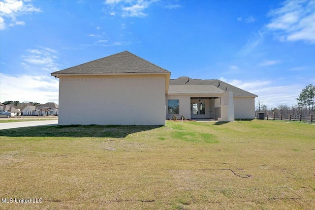 rear view of house featuring a lawn and stucco siding