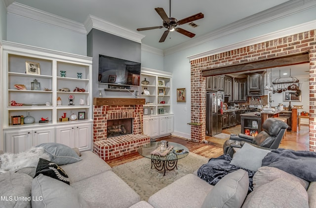 living room with brick wall, a fireplace, ornamental molding, ceiling fan, and light hardwood / wood-style flooring