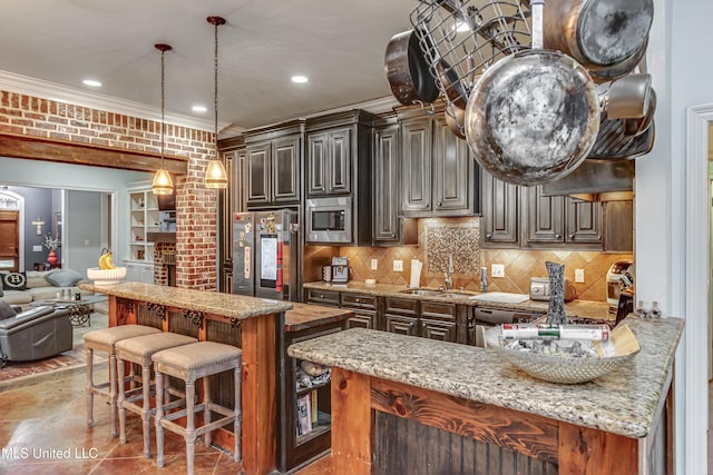 kitchen with pendant lighting, dark brown cabinetry, light stone counters, stainless steel appliances, and crown molding