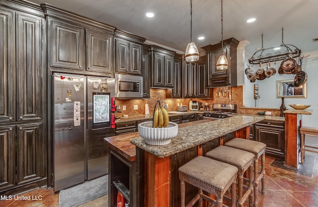 kitchen featuring stainless steel appliances, dark brown cabinetry, a kitchen island, decorative light fixtures, and dark stone counters